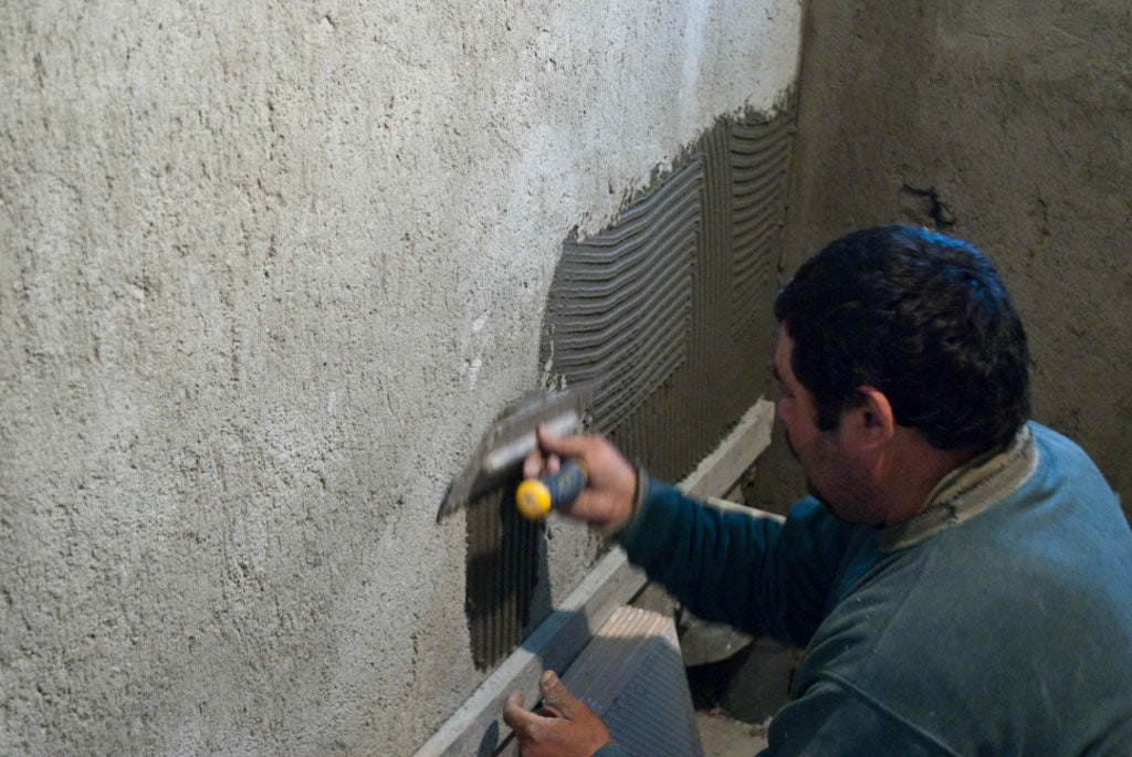Applying tile adhesive on plaster using notch trowel.